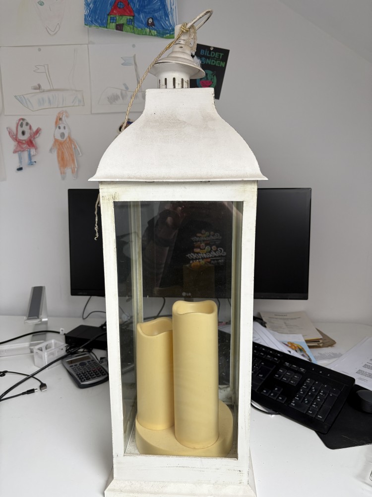 Weiße Laterne mit LED Kerzen steht auf einem Schreibtisch. Im Hintergrund ist ein Monitor zu sehen