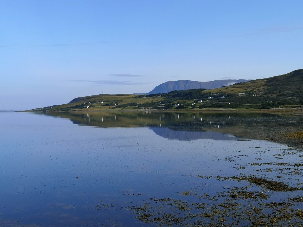 Blick auf das Loch Broom und die Berge im Hintergrund bei Ullapool in Schottland.Vor uns breitet sich eine weite Wasserfläche aus, die links in den Atlantik mündet, Rechts ist das Ufer des Mainlands, das sich mit Berge nach rechts außen erhebt
