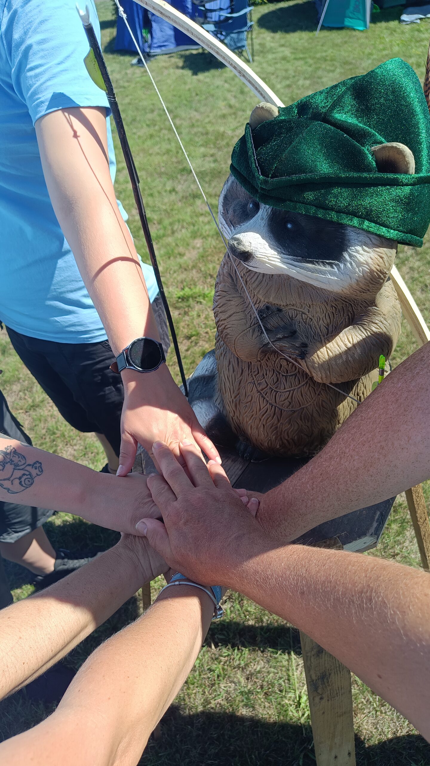 Das Camp Maskottchen in Form eines Waschbären ist zu sehen udn auf dem Podest liegen viele Hände übereinander
