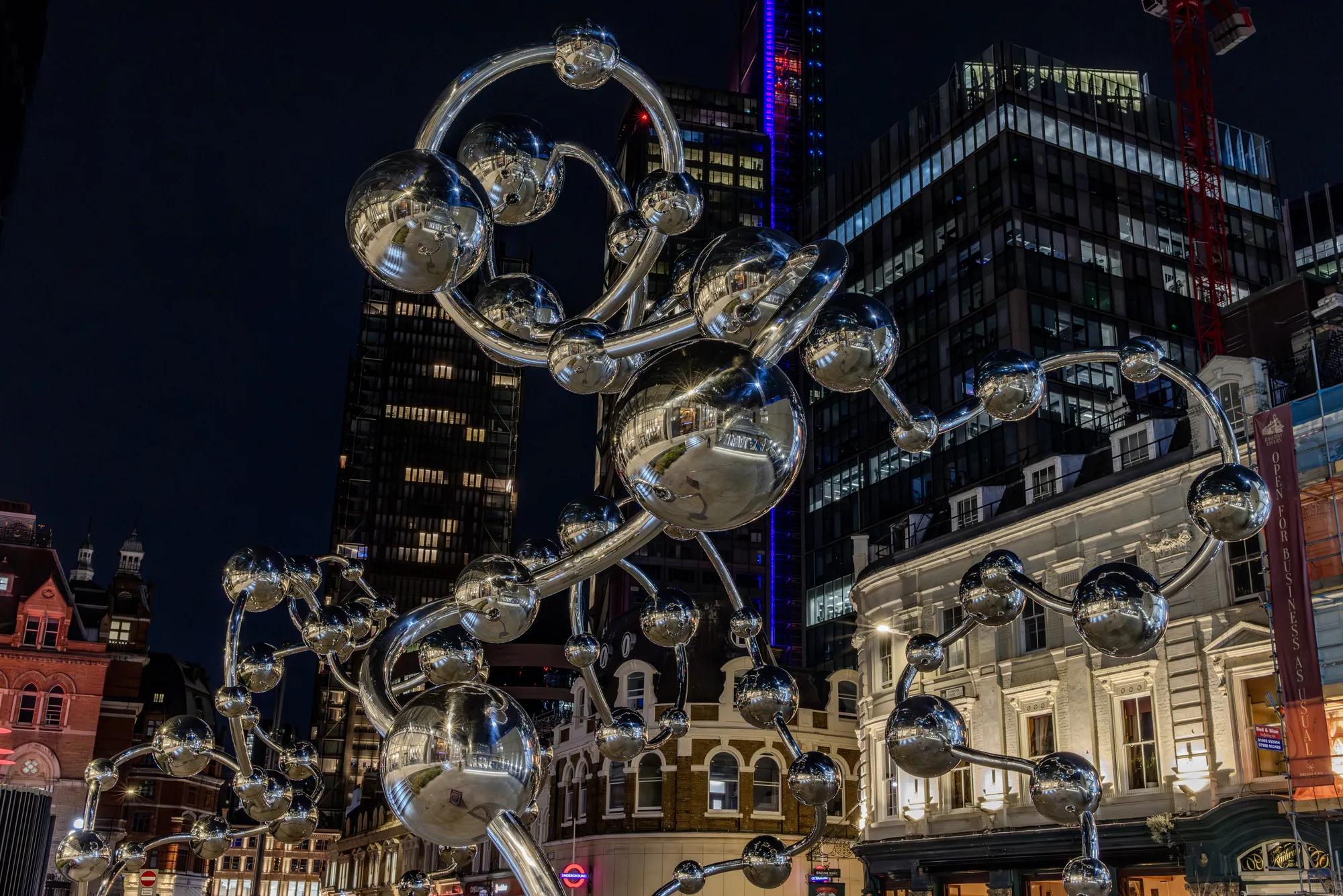 Yayoi Kusama’s polished silver sphere sculpture Infinite Accumulation arching above the public space outside Liverpool Street station’s eastern Elizabeth line entrance in London at night