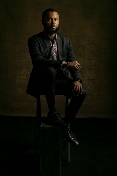 Justin Blakely sits with his arm draped over his leg in a suit