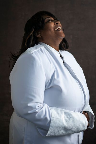 Reverend Adrian Goodrich throws her head back laughing in a white robe