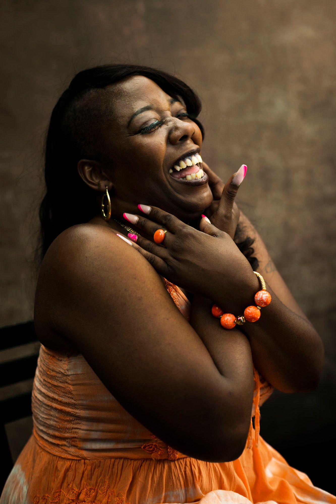 Enijua Williams laughs warmly and holds herself in an orange dress