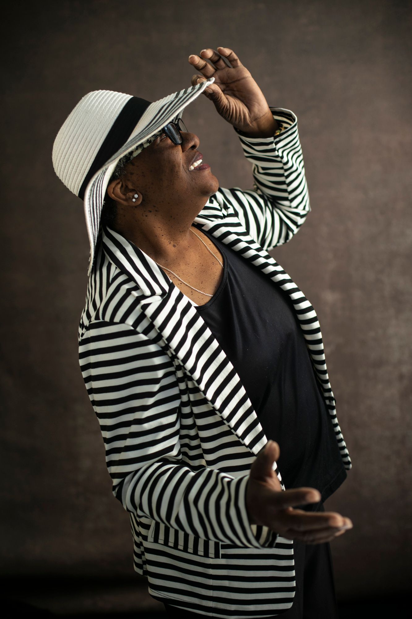 Mary Anderson smiles, looking upward, in a striped coat and hat, which she squeezes with her left hand