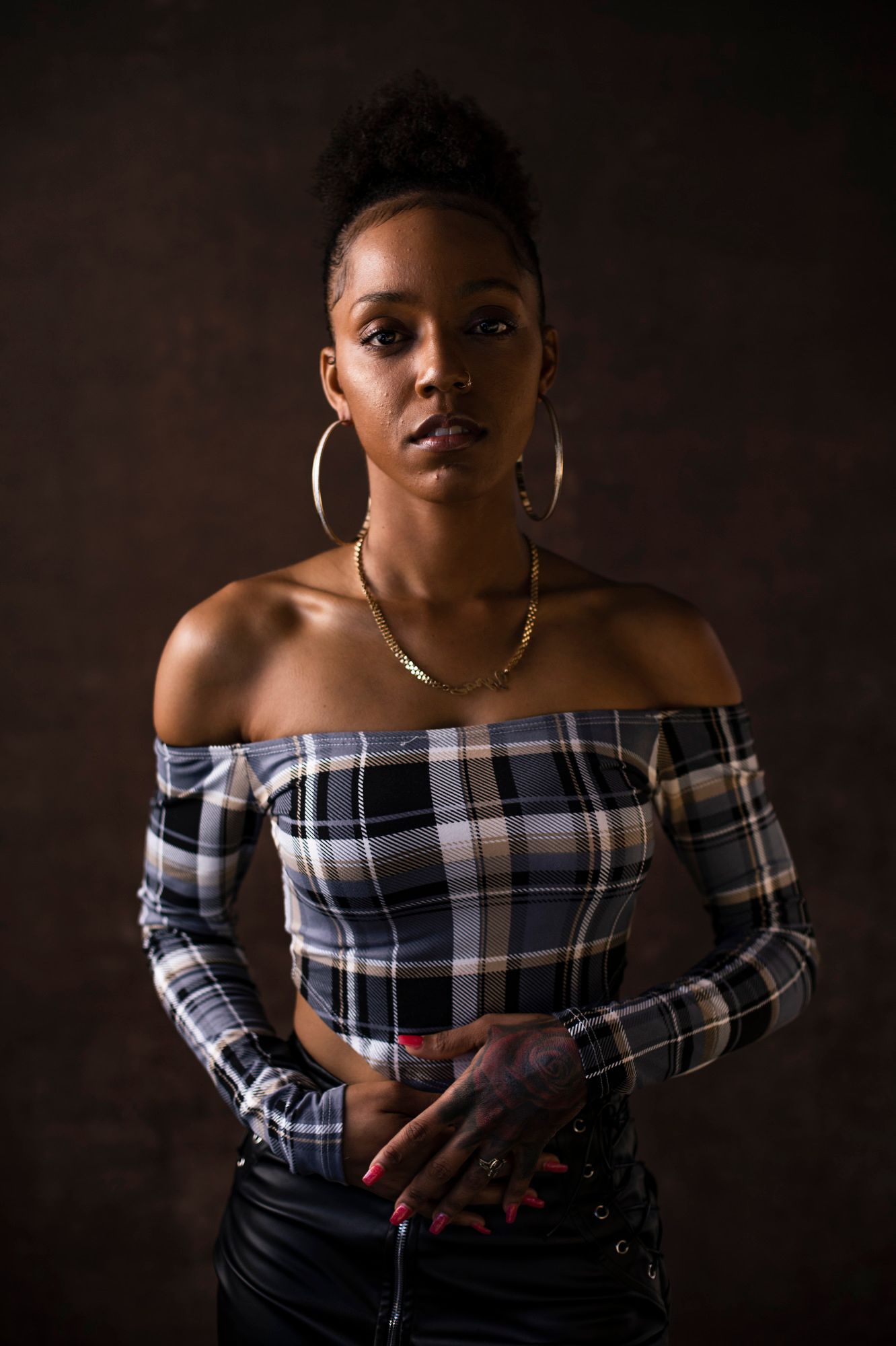 Megan stands facing the camera with her hands across her, in a shoulderless top and hoop earings
