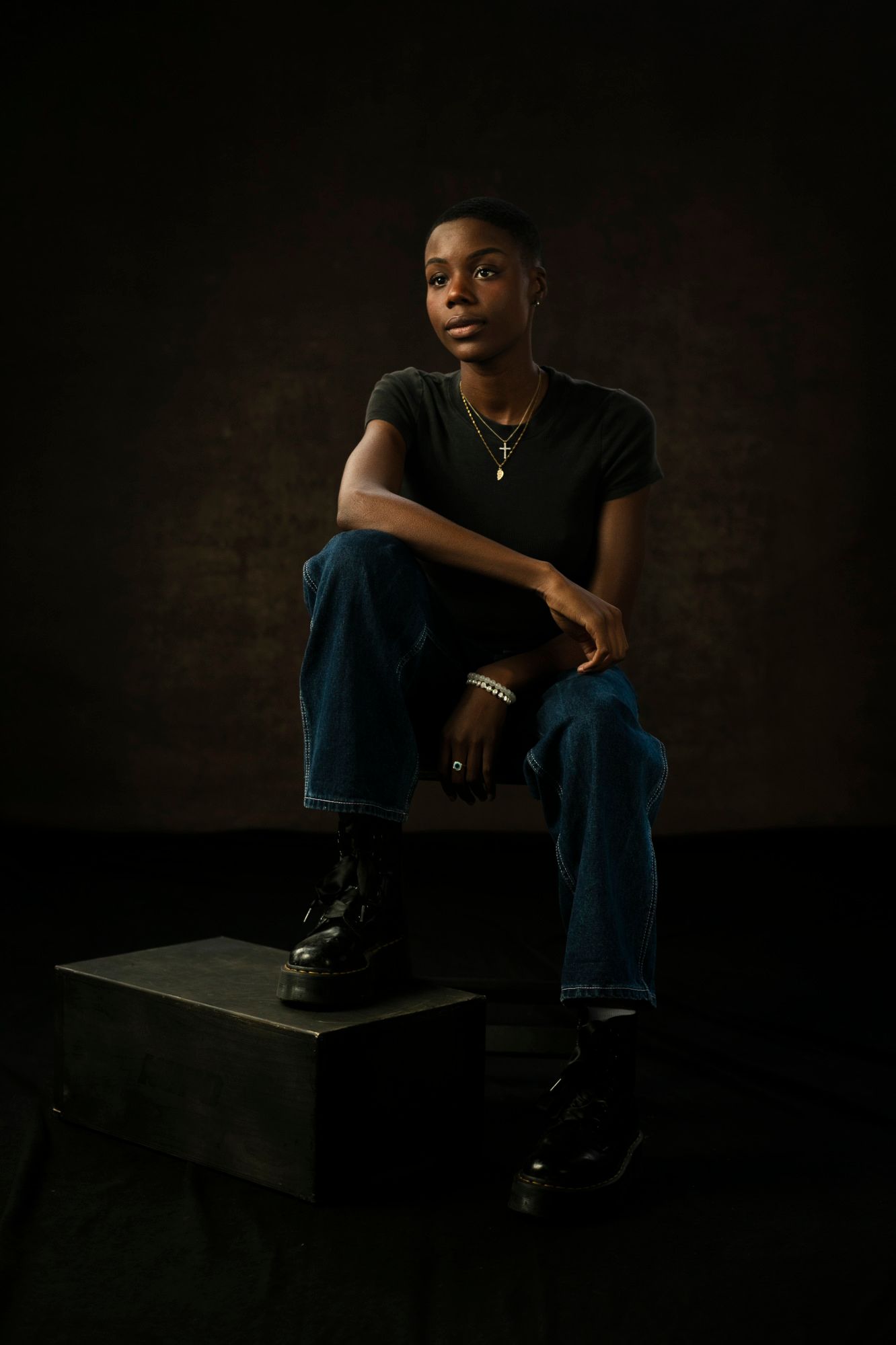 Gogo sits with their elbows propped up on their legs in big jeans and jewelery