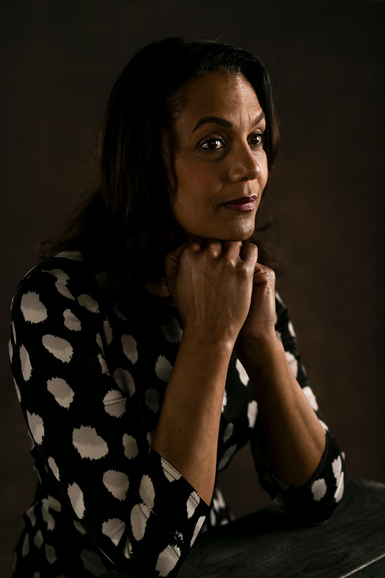 Lisa Pecot-Hebert sits in a black and white polka-dotted shirt with her hands folded under her chin