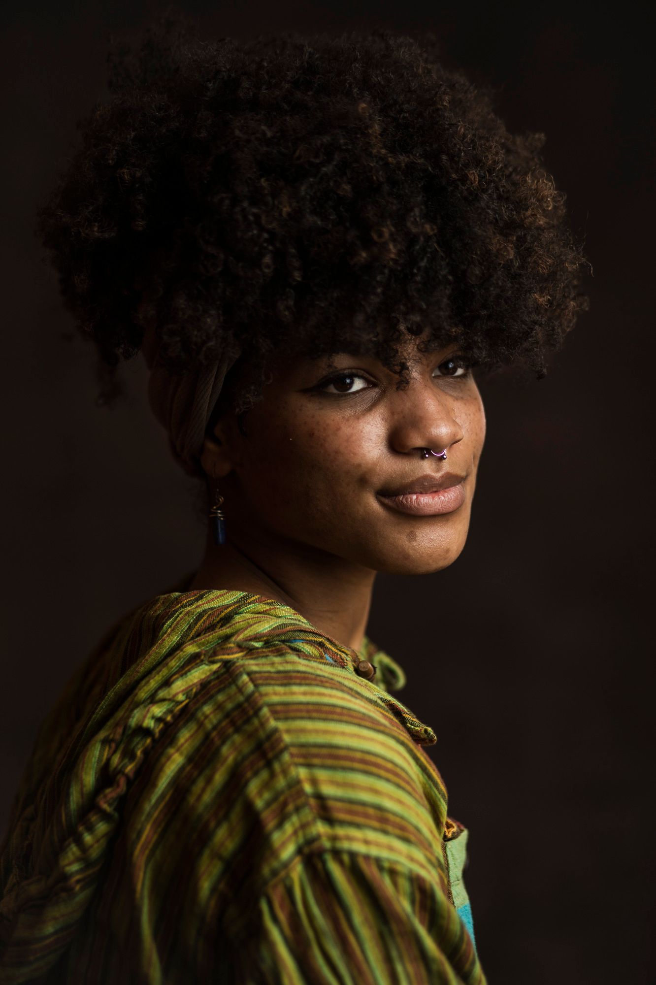 Margaux Gibson tilts their head to the camera wearing a nosering and a green striped shirt